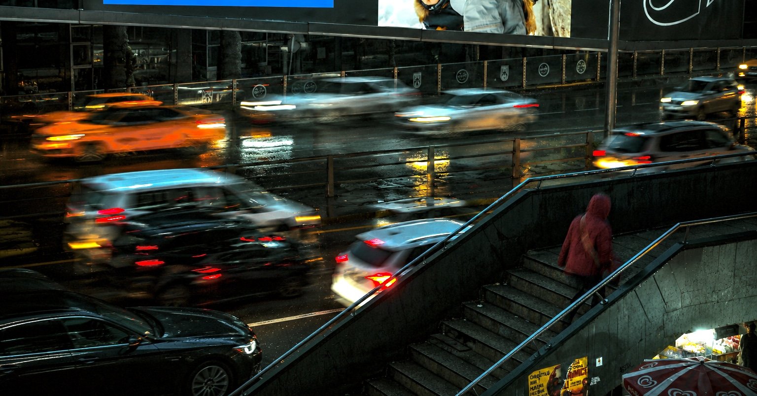 City in motion at night — cars in long exposure, commuters on the move